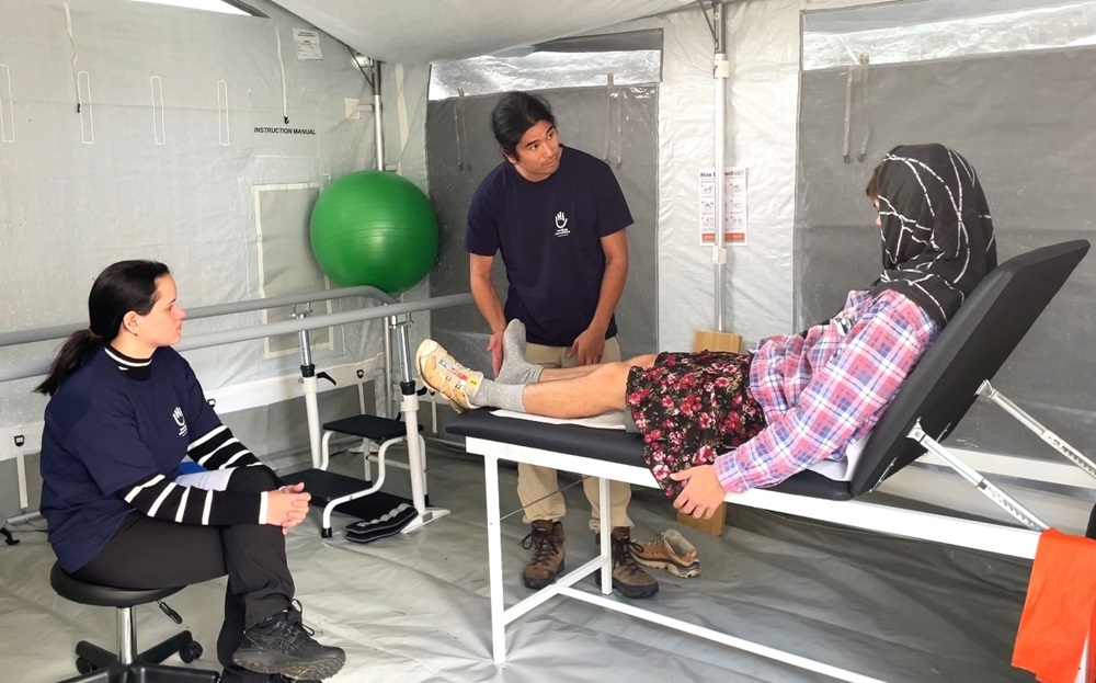 Un kinésithérapeute de HI examine un patient allongé sur une table d'auscultation.