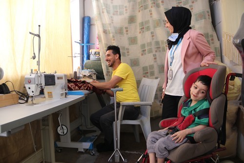 Le personnel de HI rend visite à Ahmad et à l'un de ses enfants dans son atelier de couture à domicile. © D. Ginsberg / HI