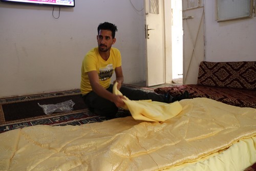 Ahmad shows bedding he made in his home-based business. © D. Ginsberg / HI