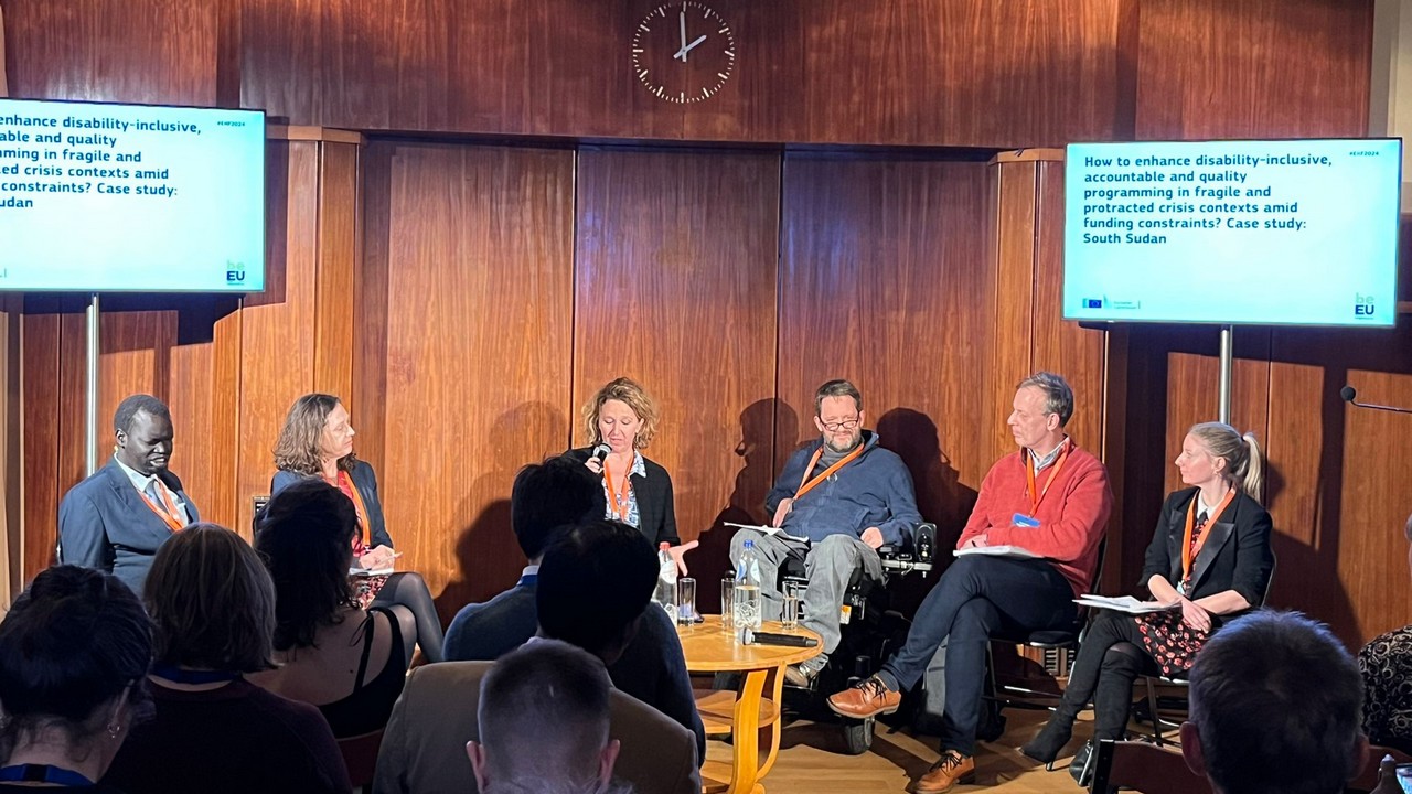 Panel of six, one black man, two white men and three white women. They are seated on chairs, one of the men is a wheelchair user. They discuss the following topic: how to enhance disability-inclusive, accountable and quality programming in fragile and protracted crisis contexts amid funding constraints? Case study: South Sudan.