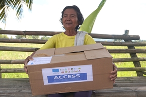 Une dame aveugle est assise sur un banc et porte dans ses bras un carton d'aide humanitaire 