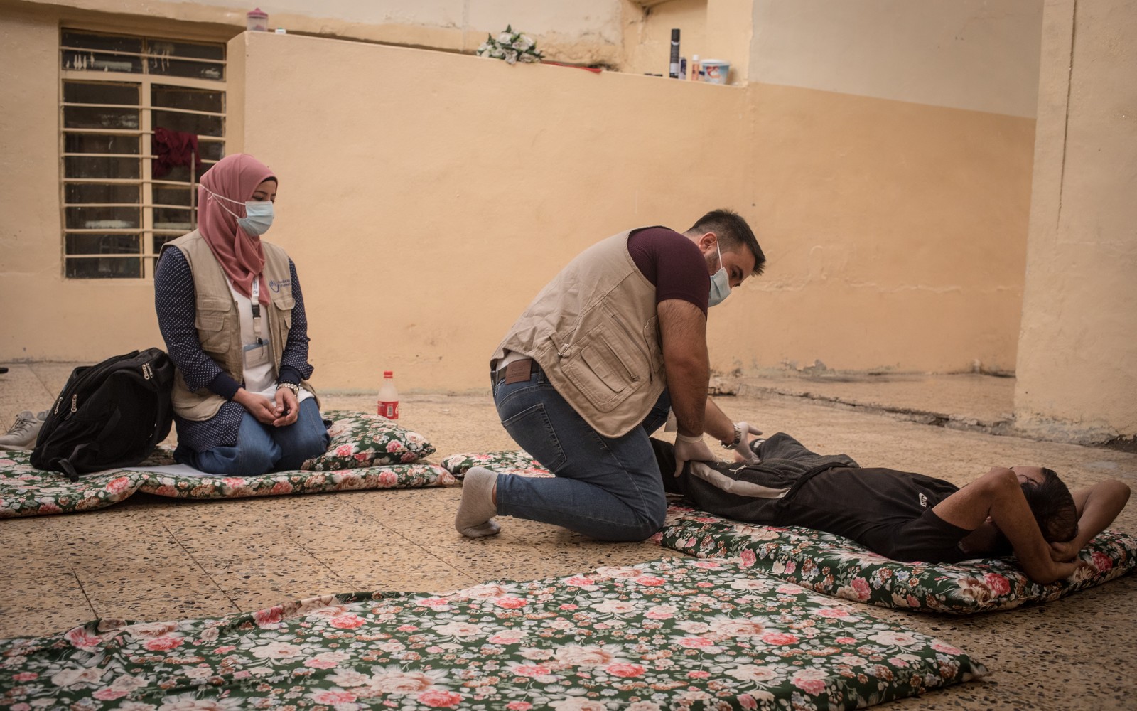 A patient lying down is treated by a physiotherapist who gives him exercises.