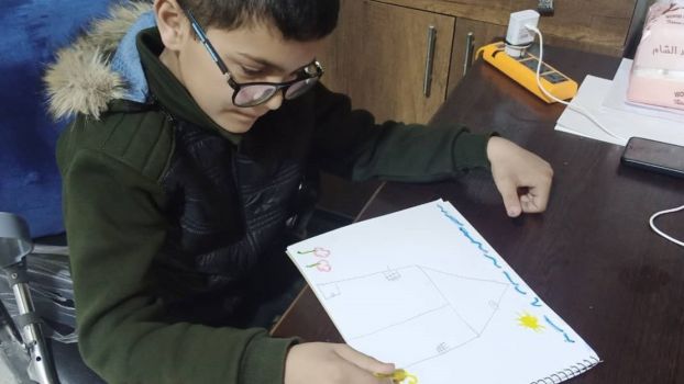 Un petit enfant syrien fait un dessin sur lequel on voit une maison et un soleil ; }}