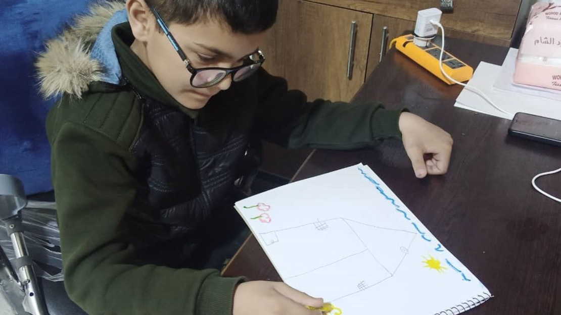A little Syrian child draws a picture of a house and a sun 