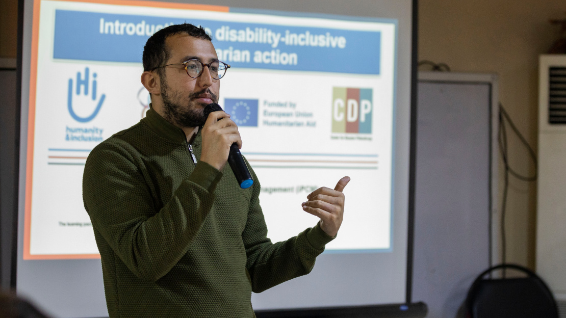A man giving a presentation to an audience in Syria.; }}