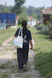 Ambika, marchant sur un chemin avec un sac et un t-shirt HI. © A.Thapa / HI