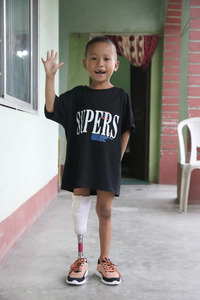 Prabin se tient debout avec sa nouvelle prothèse et salue le photographe en souriant. © A.Thapa / HI