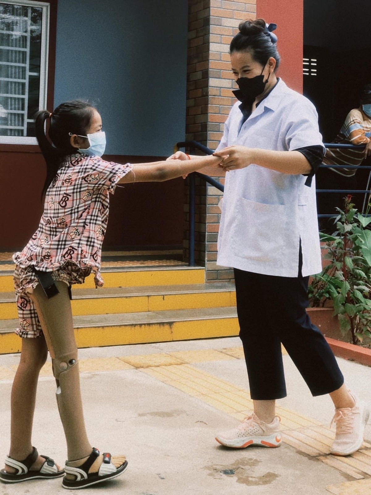 Rakseymutta tient les deux mains d'une petite fille avec une prothèse pour 'laider à marcher