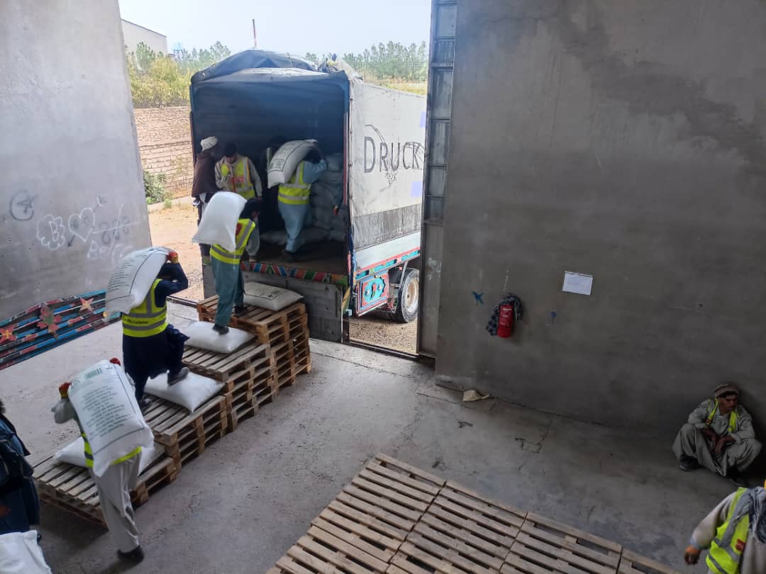 On a loading platform, several men carry large bags on their backs and place them in a lorry.