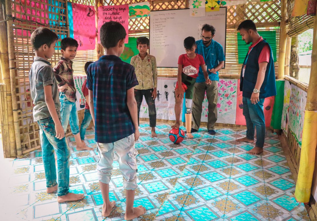 Jubair, entouré de plusieurs autres jeunes réfugiés rohingyas dans une salle, guidé par les équipes de HI pour reprendre confiance et jouer au foot avec sa prothèse 