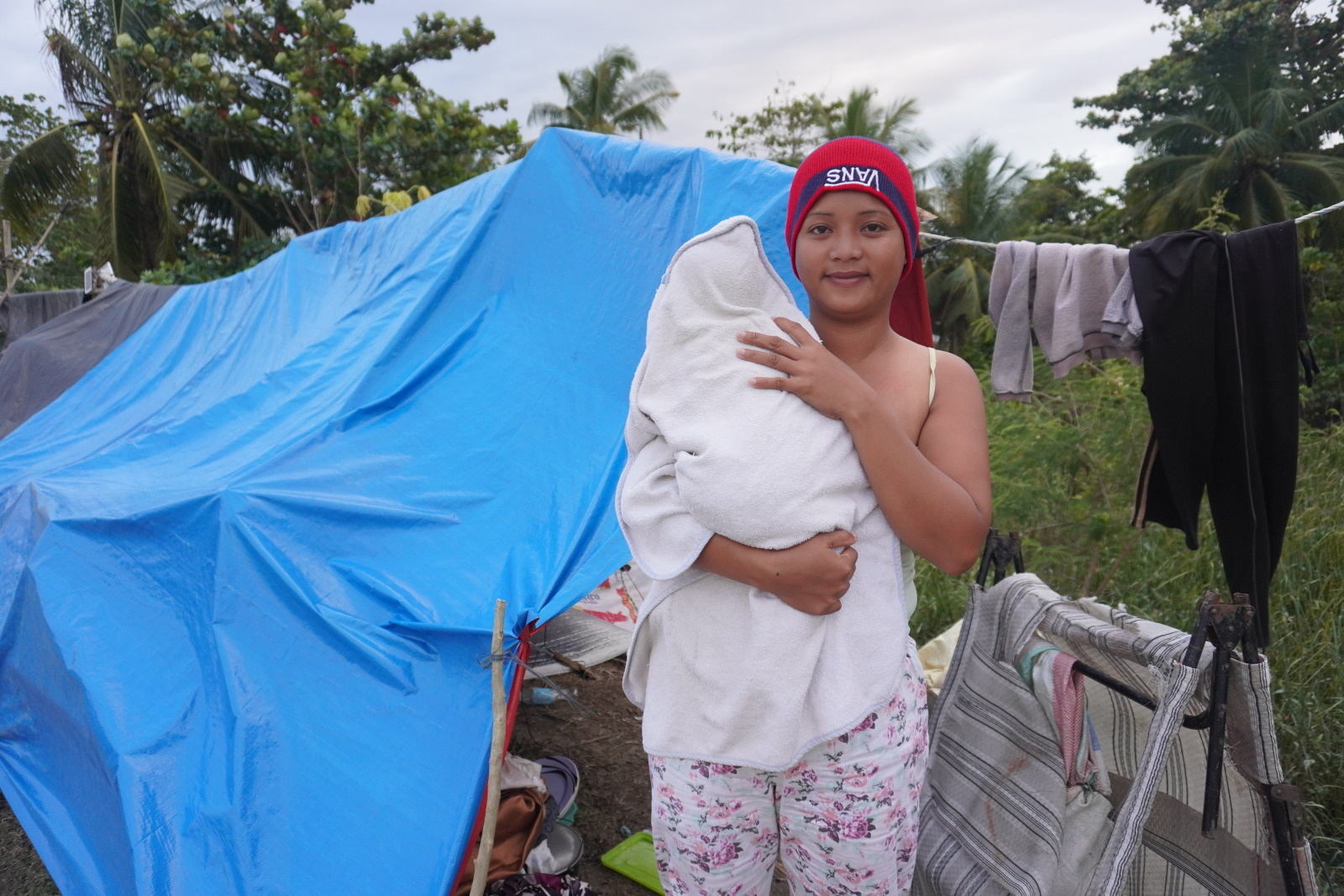 Charlyn and her baby in front of their flooded shelter in the town of Carmen, Davao del Norte. © Maria Clarissa Manalastas / HI