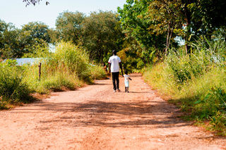 Un père et sa fille marchent sur la route qui mène à l’école de Bissine © A. Faye / HI