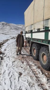 A man stands next to a lorry on a snow-covered road.