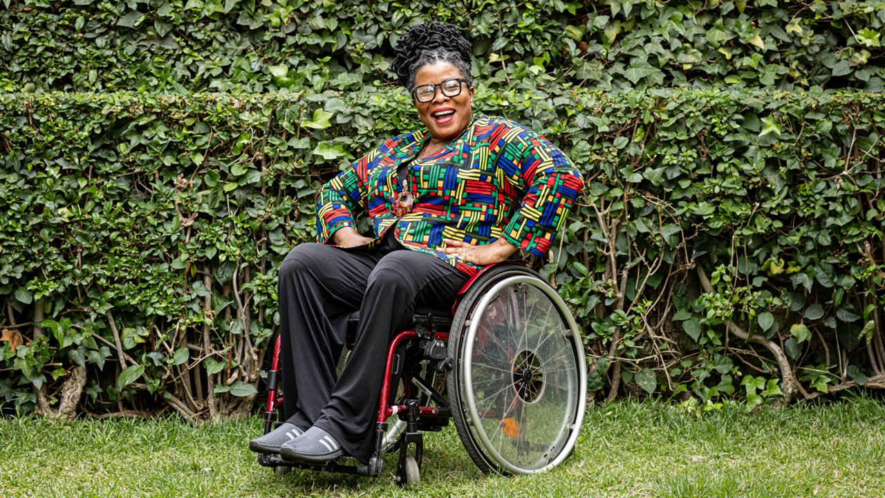 Femme souriante en fauteuil roulant qui pose pour la photo dans un jardin.