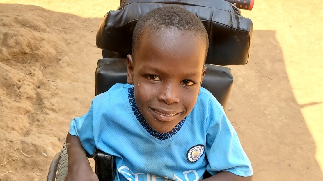 Portrait en gros plan d'un jeune garçon assis dans un fauteuil roulant. Il regarde l'appareil photo et sourit.; }}