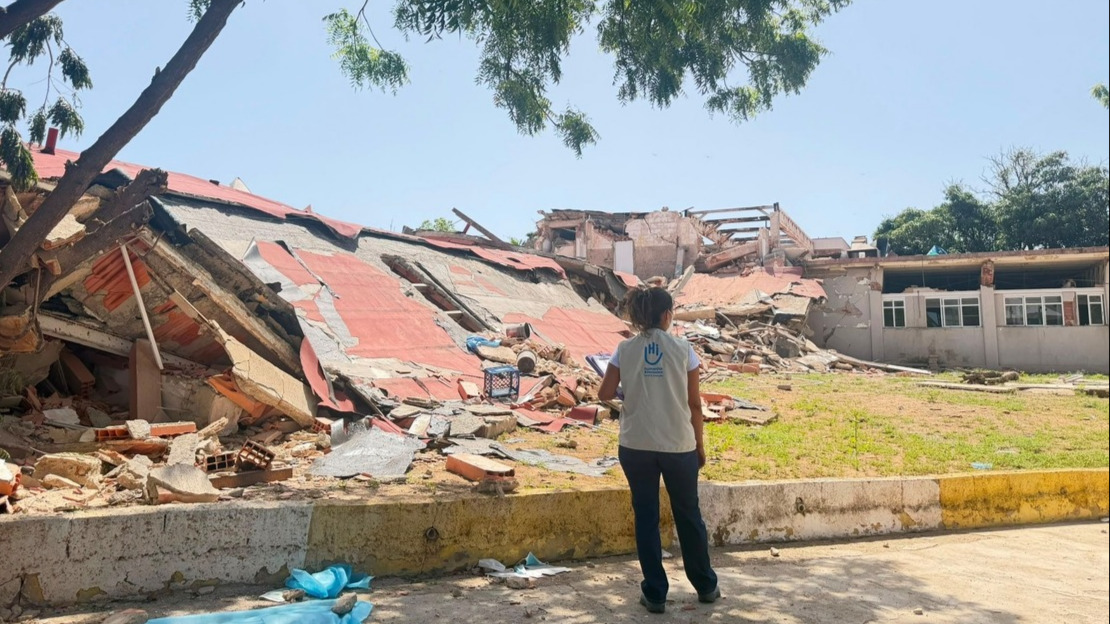 Une femme se tient de dos devant un bâtiment complètement détruit.