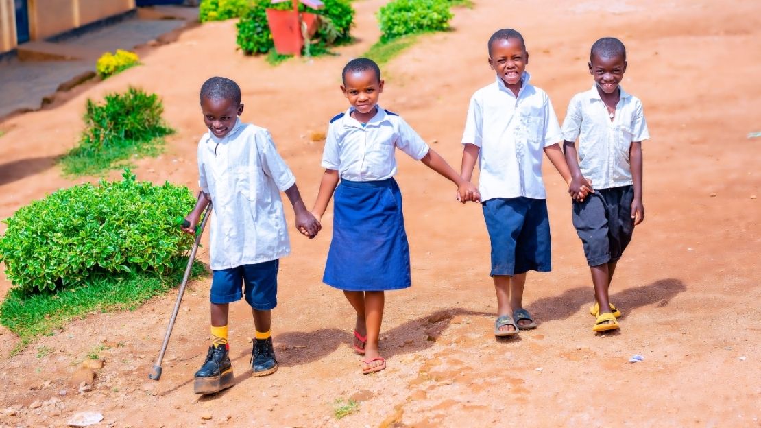 Quatre enfants en uniforme scolaire marchent main dans la main. Le garçon à gauche sur la photo porte une chaussure orthopédique et utilise une béquille.