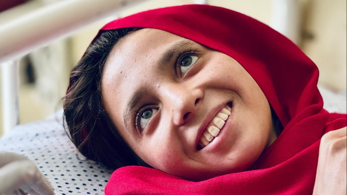 Close-up portrait of a young girl lying on a bed with a big smile.; }}