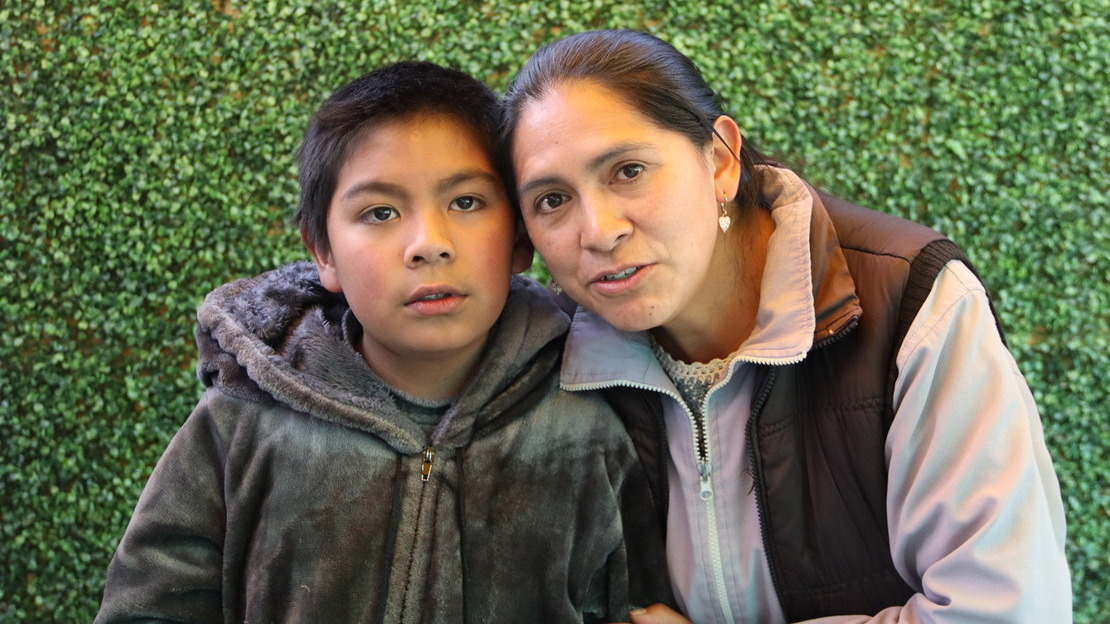 Portait en gros plan d'un garçon et de sa maman, sur fond vert. Ils se serrent tendrement l'un contre l'autre et regardent la caméra en souriant.; }}