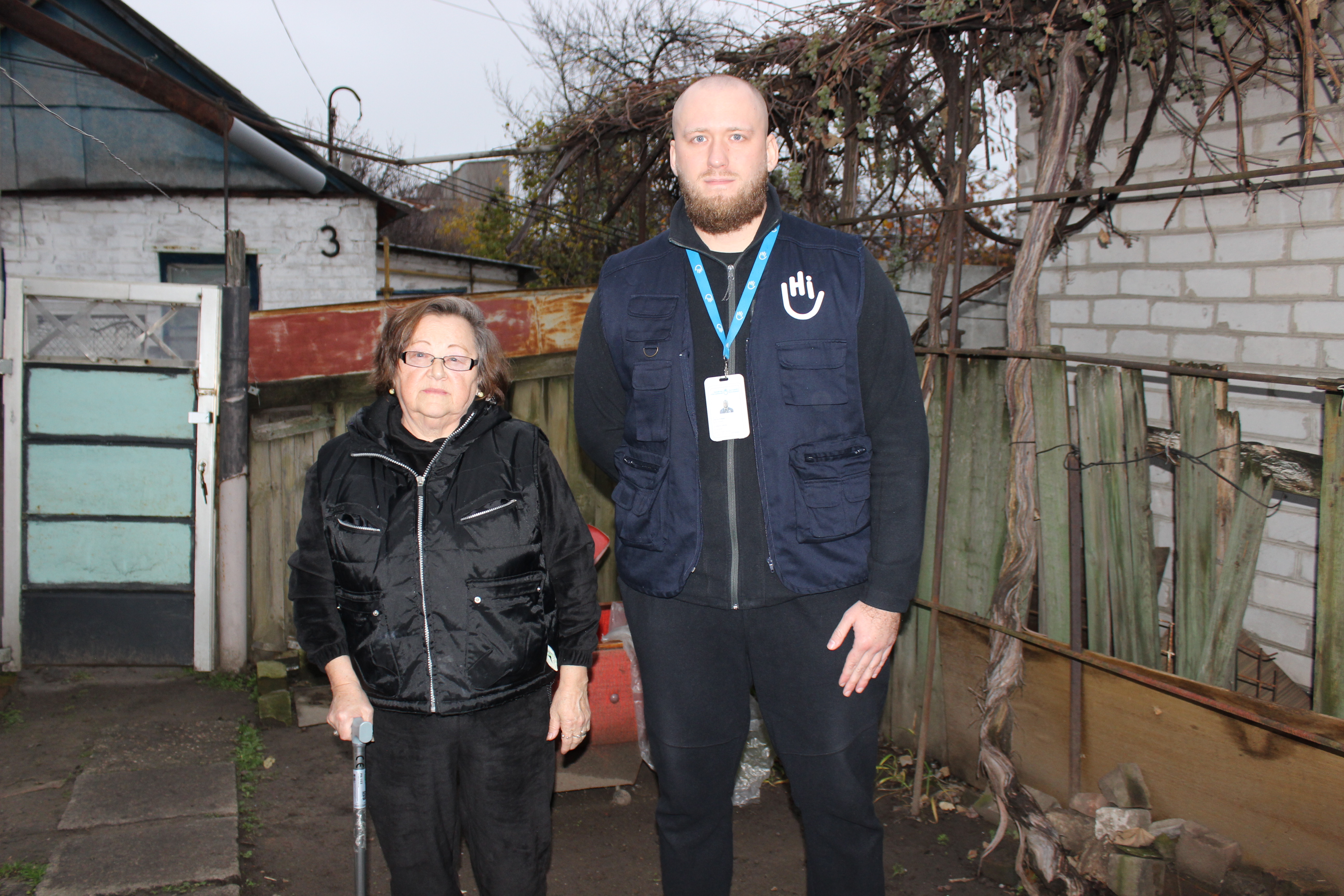 Valentyna Dukh, près de son logement fourni par la communauté, en compagnie d'Artur Chumak, travailleur social de HI. Dnipro, novembre 2025; }}