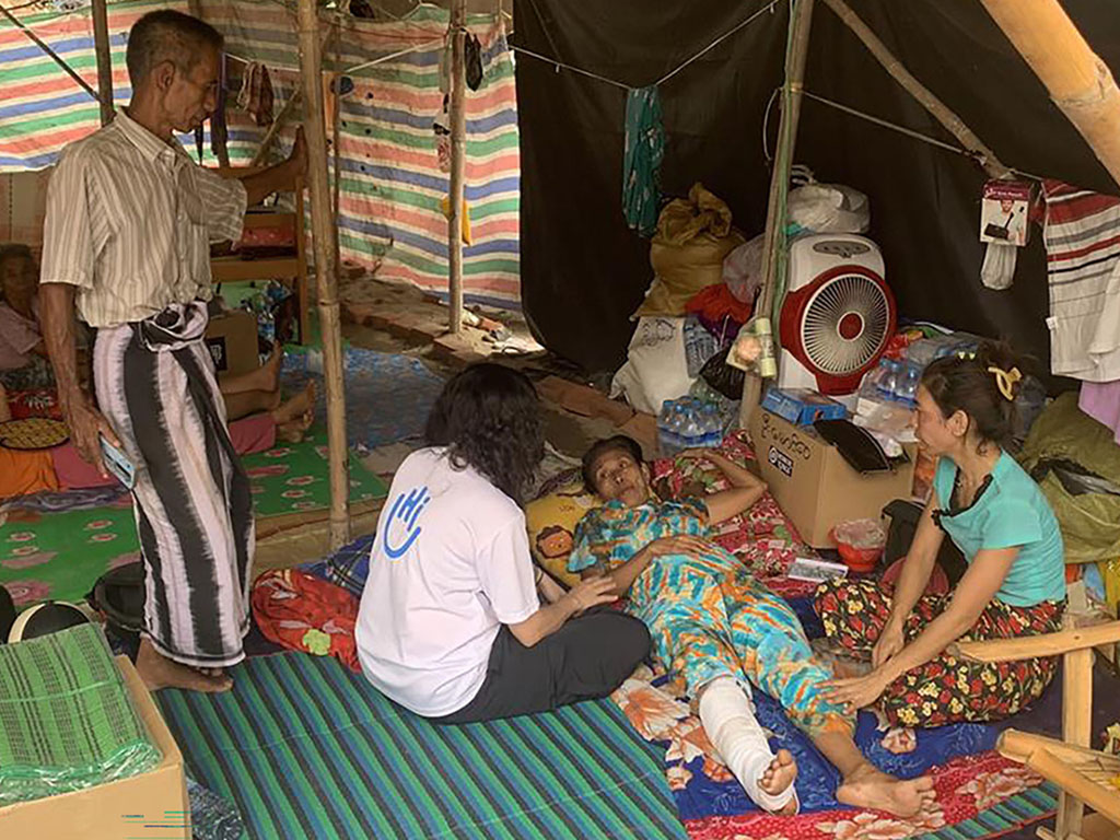 The woman lay down with her leg in a cast under a shelter speaking to people.; }}