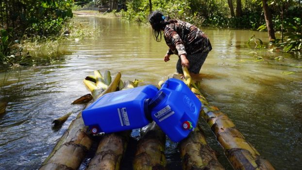 Une femme doit traverser les terrains inondés pour rejoindre sa maison avec les bidons d’eau et les kits d’hygiène fournis par HI dans le cadre de sa réponse d’urgence. 500 ménages touchés par les inondations ont déjà reçu le soutien de HI, dans la province de Davao del Norte.; }}