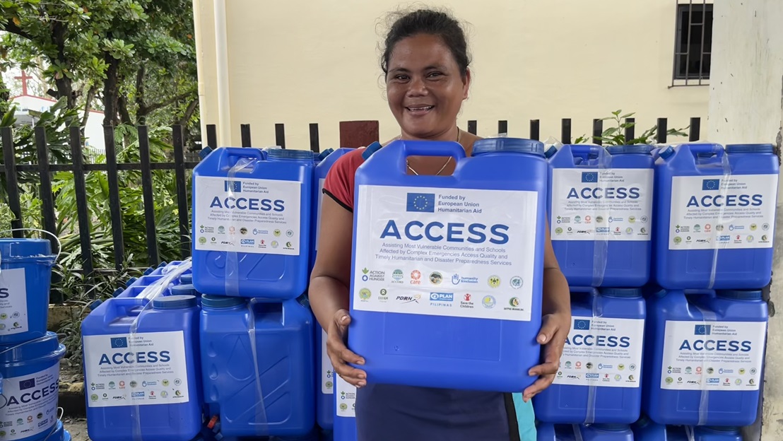 A young woman receives a jerrycan of water during a humanitarian aid distribution.; }}