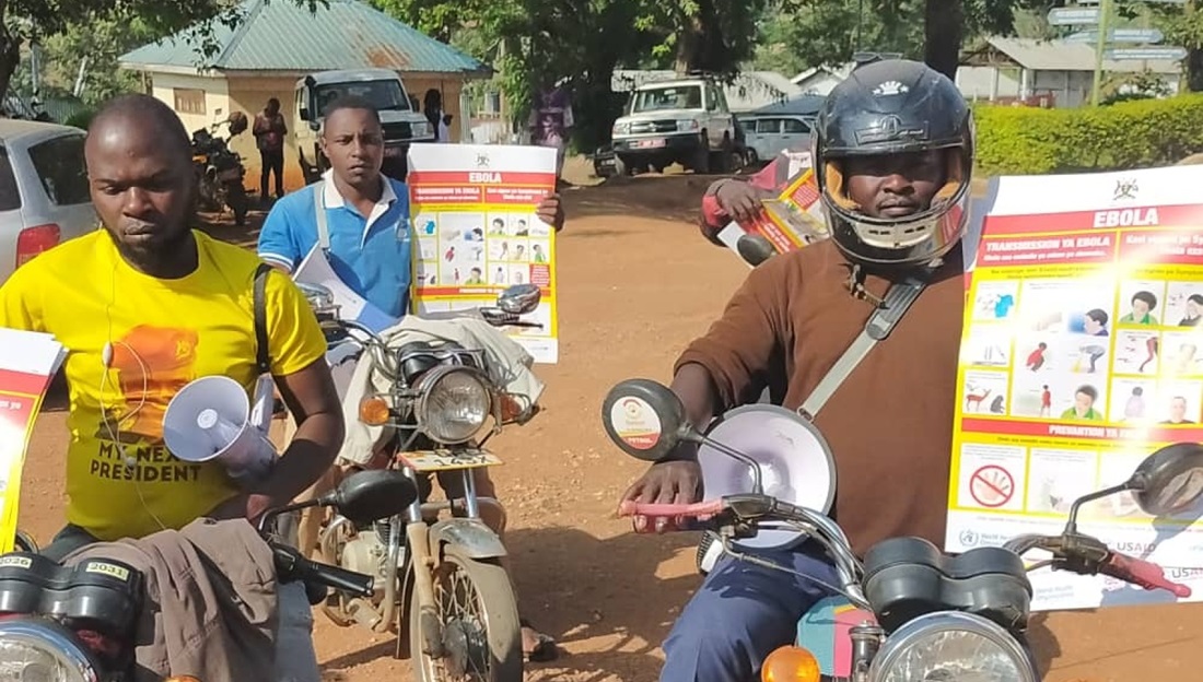 Men are riding motorbikes carrying posters raising awareness about Ebola.