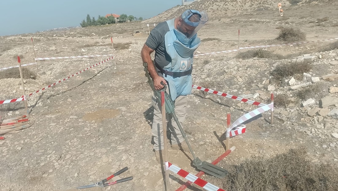 Un démineur de HI procède à la dépollution d'une parcelle identifiée comme contaminée par des engins explosifs. Il est debout et tient un détecteur.; }}