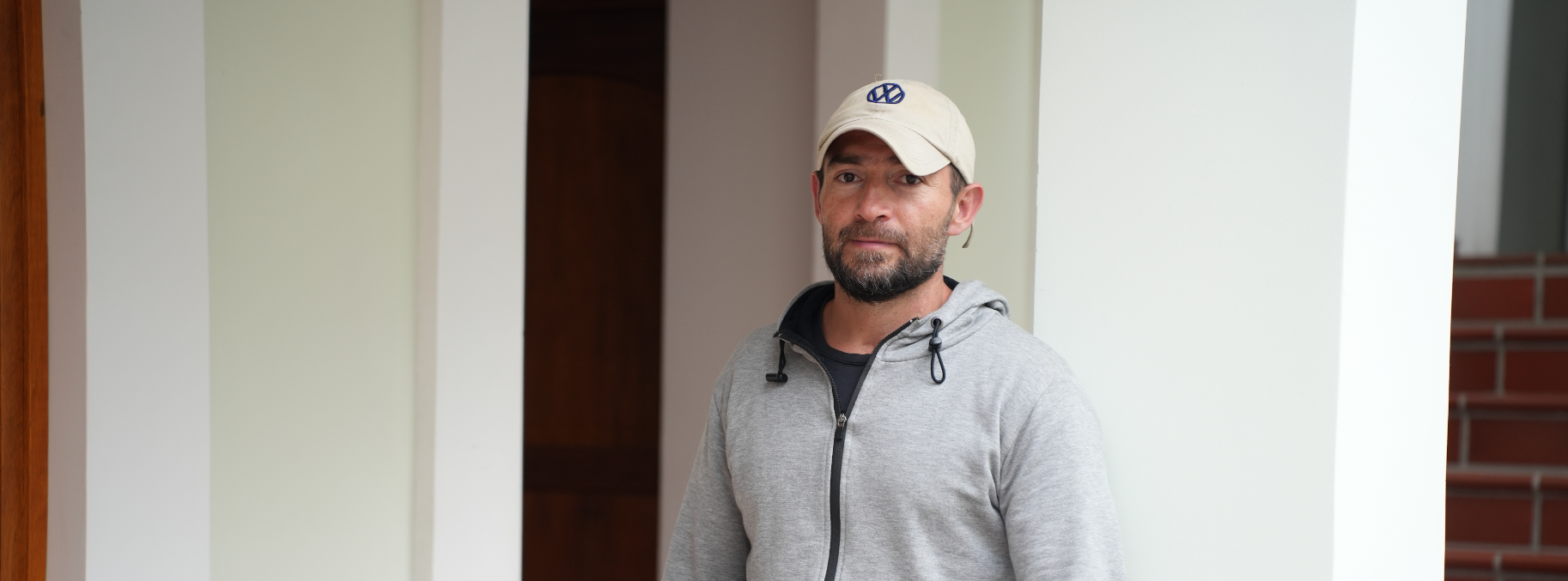 Portrait of Andres wearing a grey sweater and a white cap, standing outdoors.