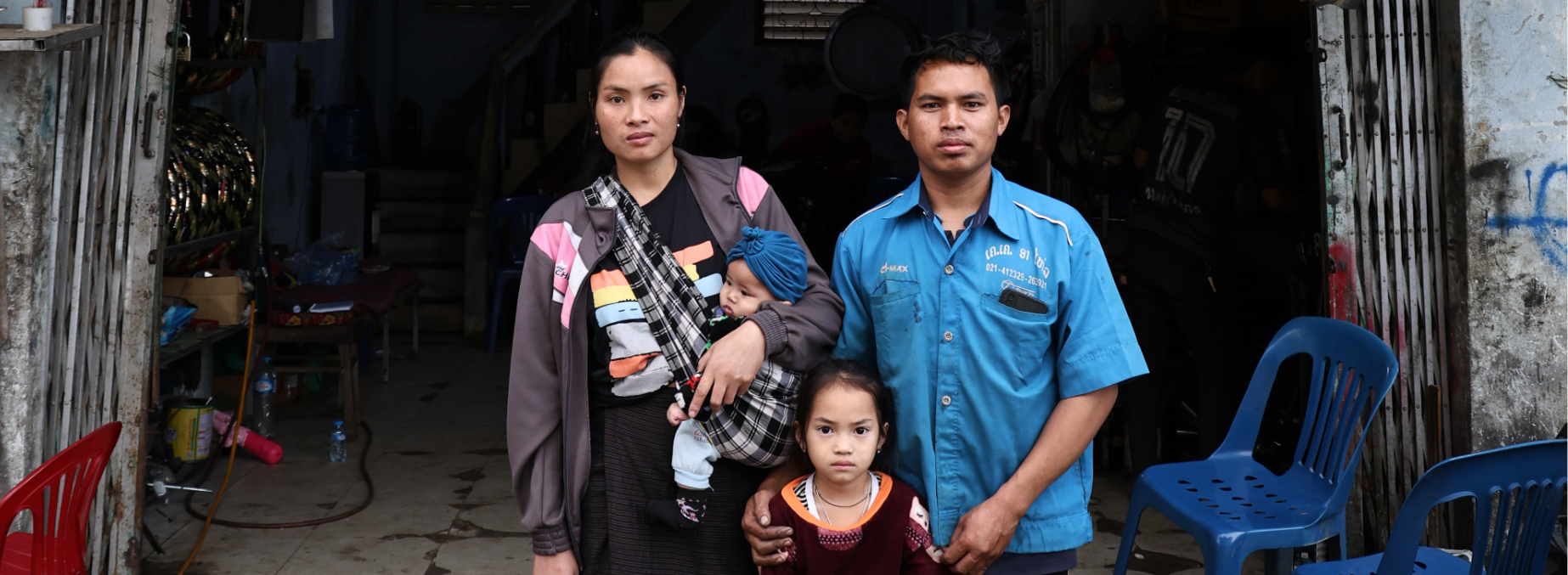 A family composed of a man, a woman and two children are standing in front of an entrance.