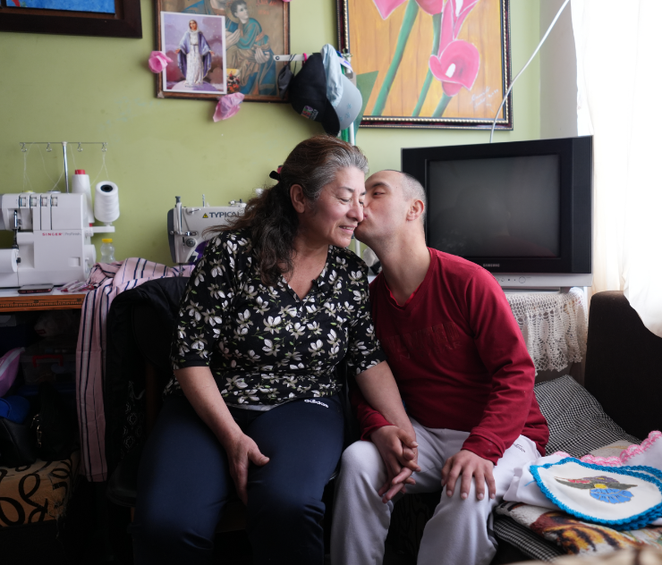 Sebastian kisses his mother’s cheek, while they are both sitting on a couch.
