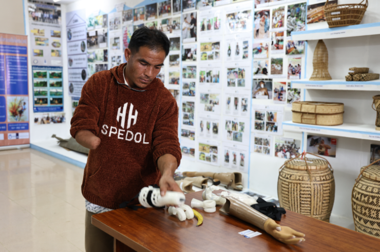 Mr Ngok stands in front of a picture wall and has a prosthetic arms in his hand.